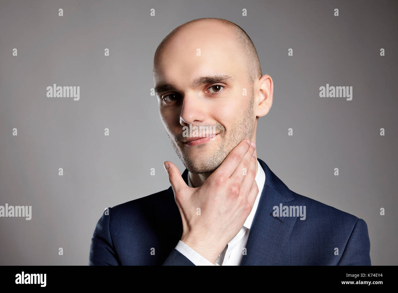 Portrait of a young man stroking his chin. Headshot on gray background. Stock Photo