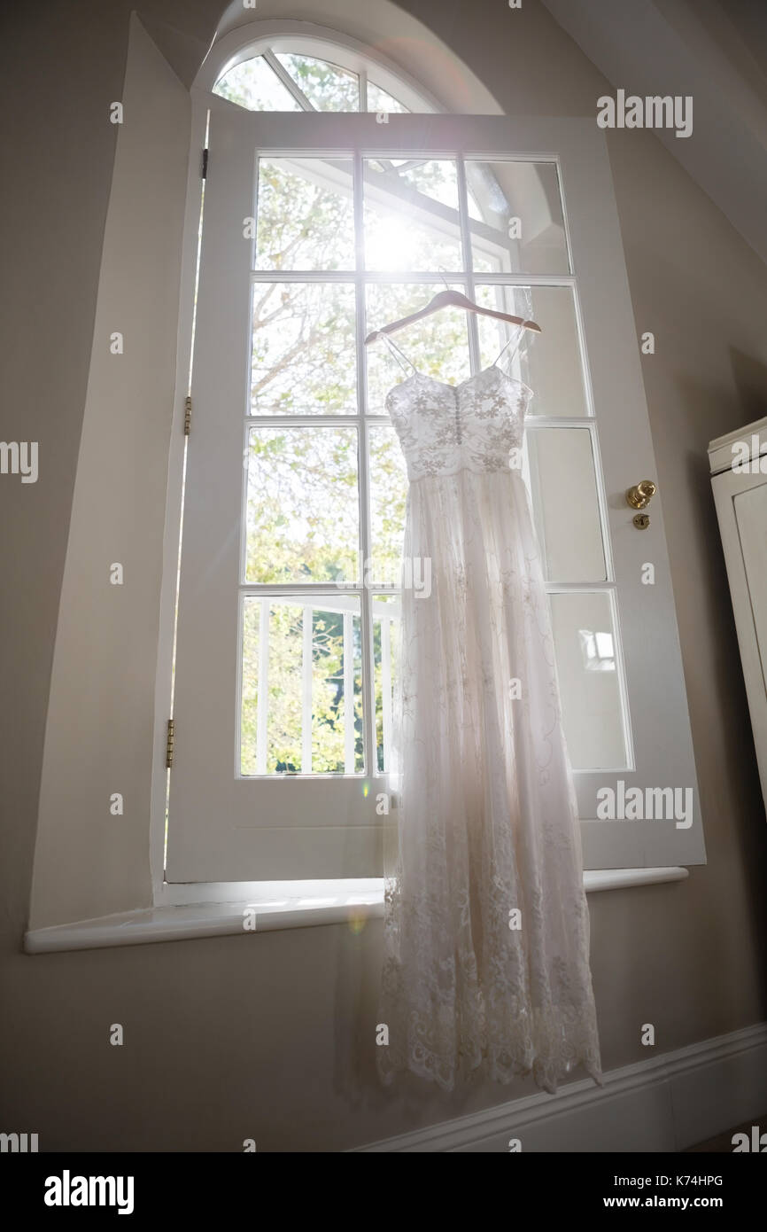 Wedding dress hanging on window in dressing room Stock Photo