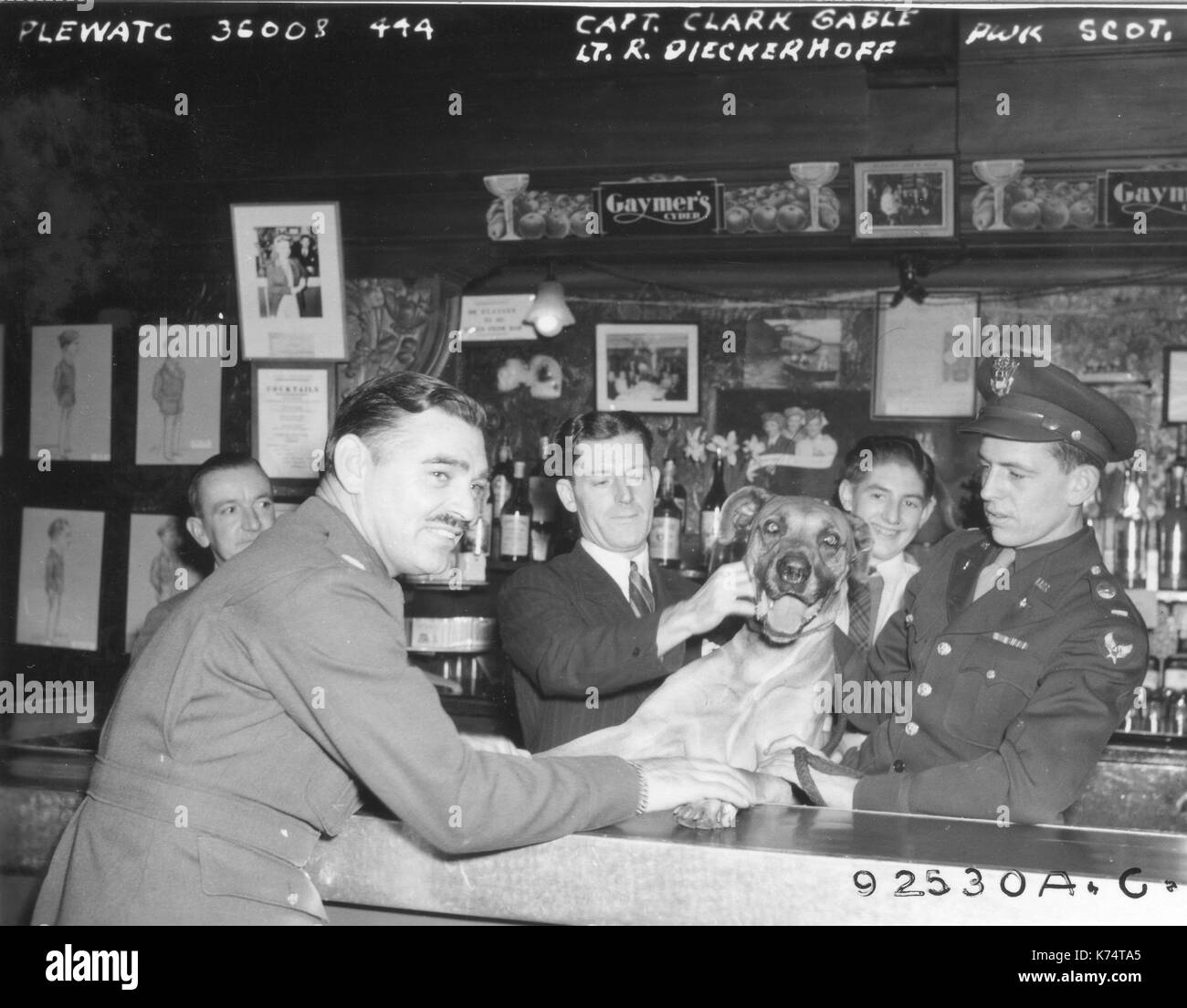 Capt Clark Gable (left) and Lt R Dieckerhoff (right) join dog and patrons at an embarkation point watering hole prior to returning to the United States, England, 1944. Stock Photo