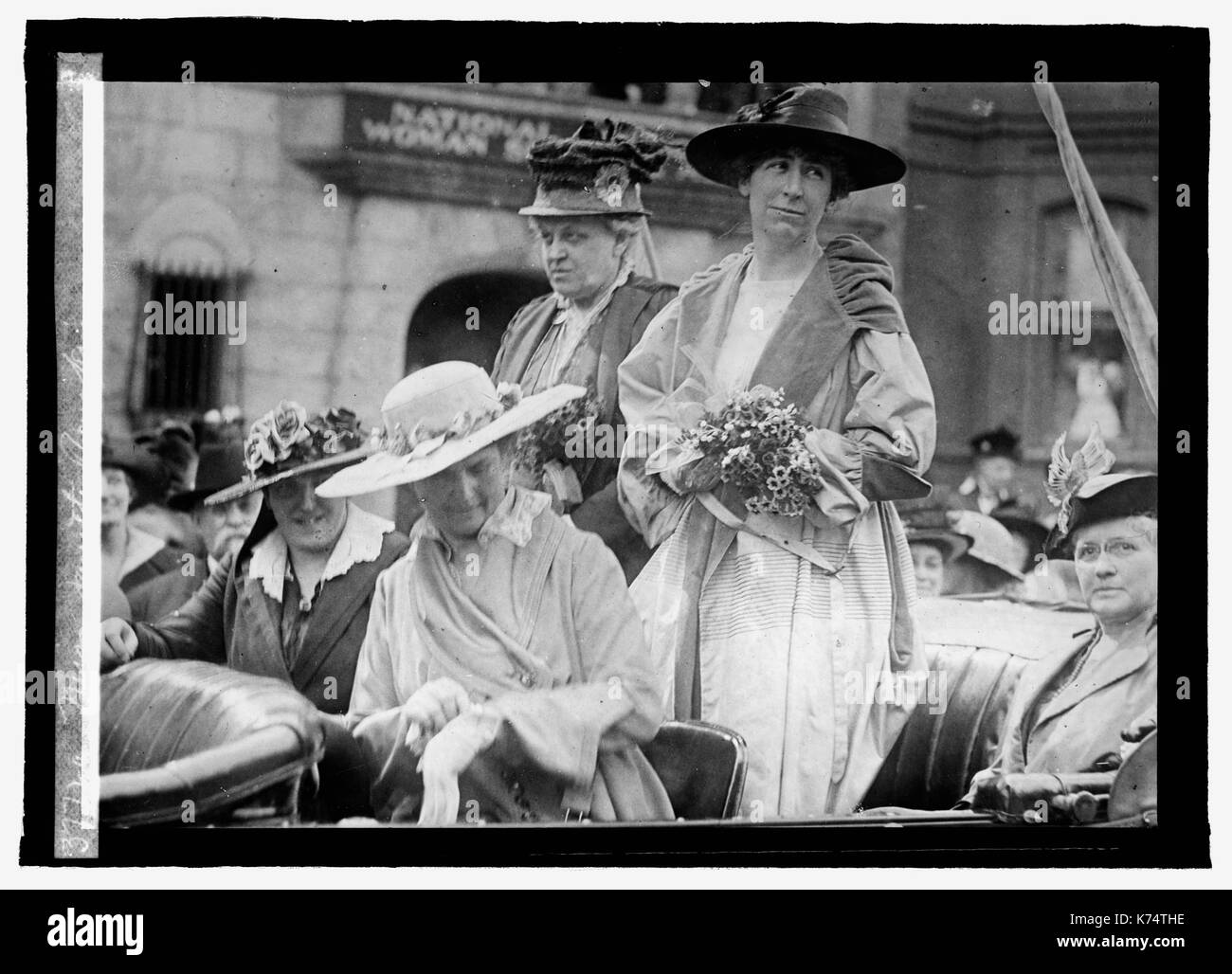 Jeannette Rankin (standing left), the first woman to hold national office in the United States, and Carrie Chapman Catt (standing right), stand in the back of an automobile outside the National American Woman Suffrage Association offices, Washington, DC, 1916. Photo by National Photo Company Stock Photo