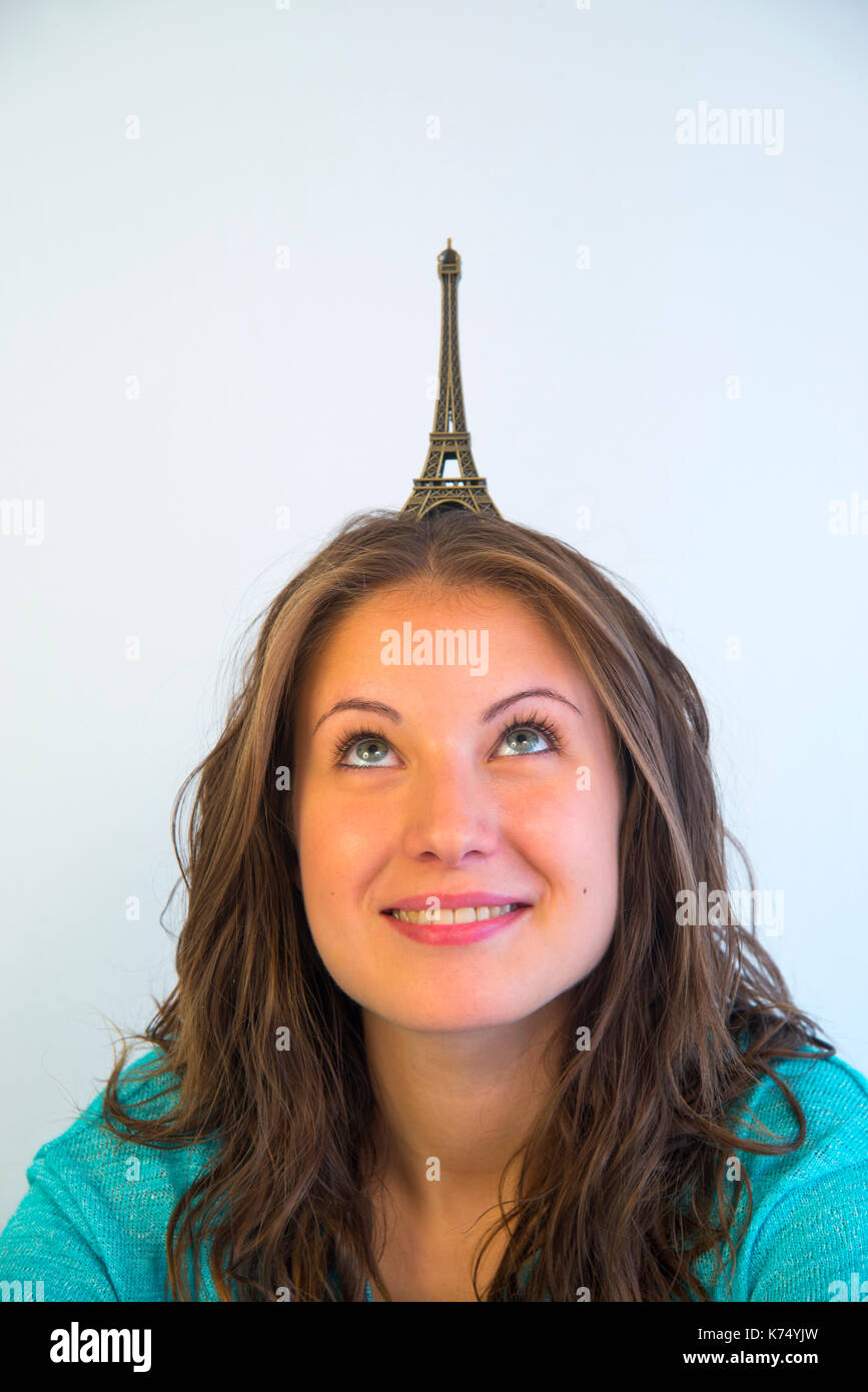 Young woman looking up, with a scale reproduction of Eiffel Tower on her head. Stock Photo