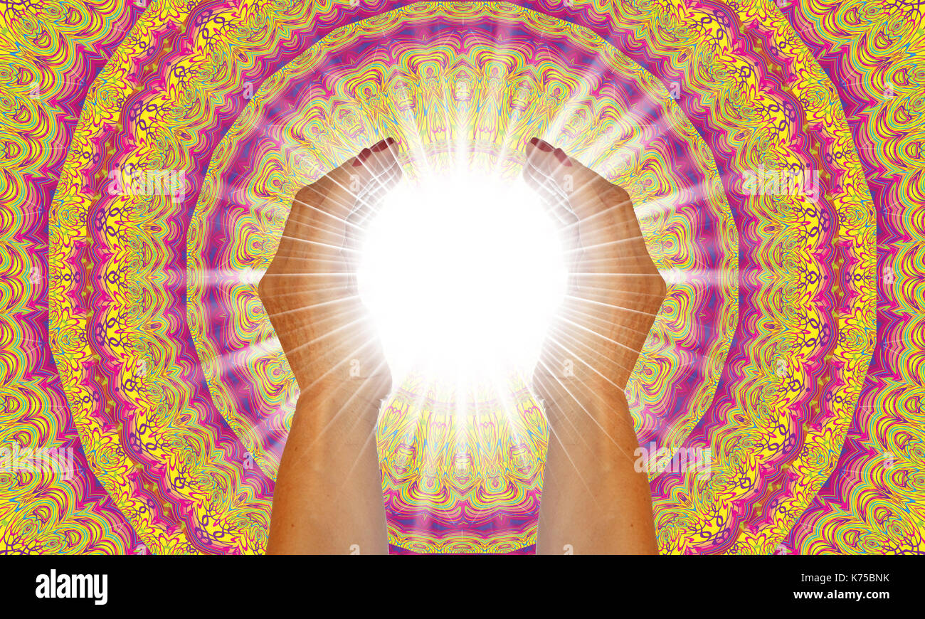Rays of white light between the hands of a woman with multicolored mandala background Stock Photo