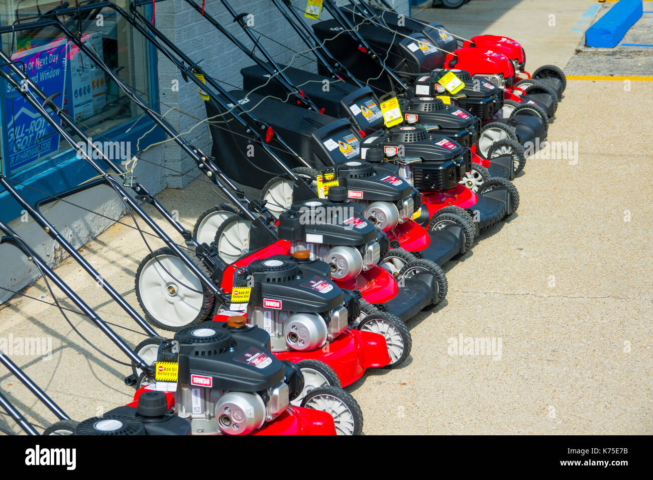 row of red hand pushed lawn mowers for sale outside of a hardware store Stock Photo