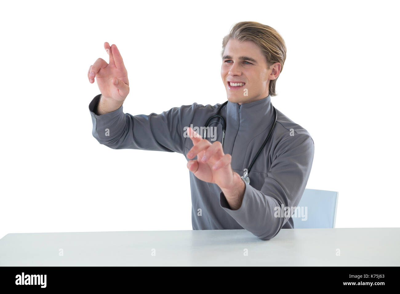 Smiling male doctor touching imaginary interface screen while sitting at table against white background Stock Photo