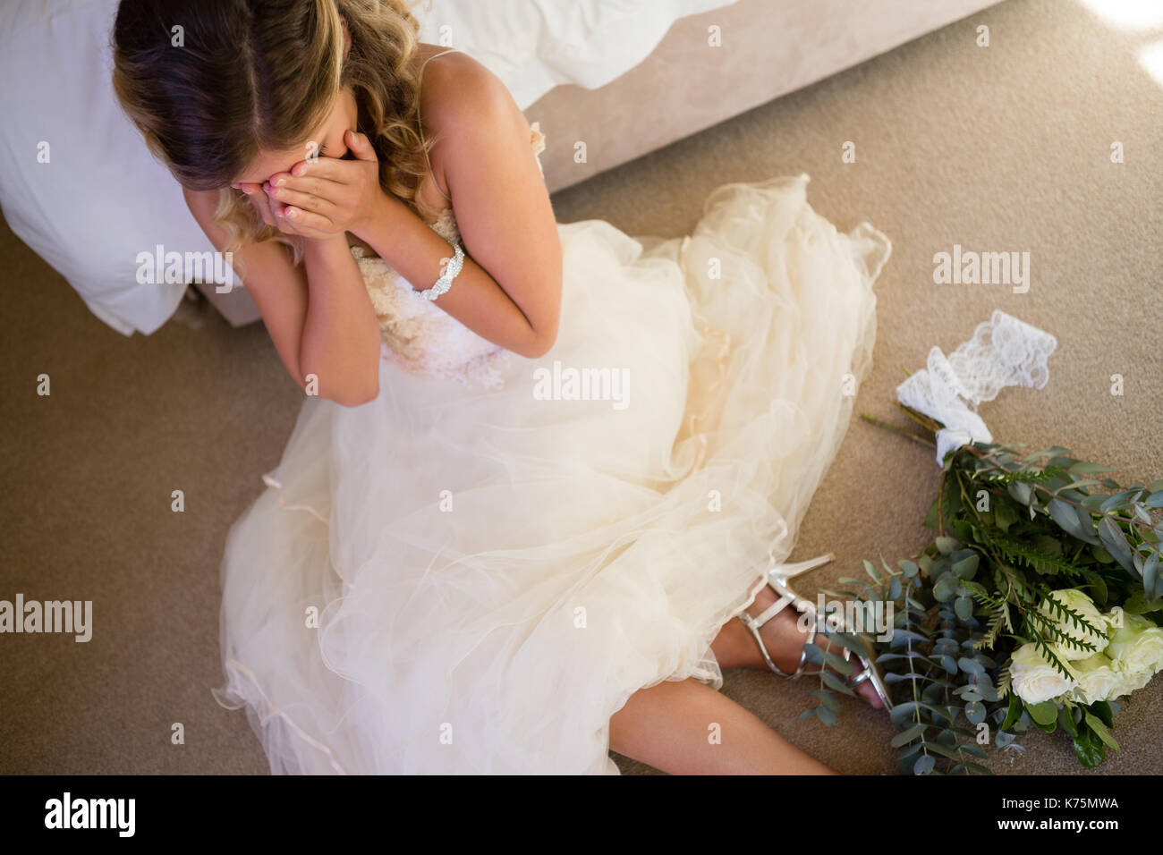 High angle view of bride in wedding dress crying while sitting by bed at home Stock Photo