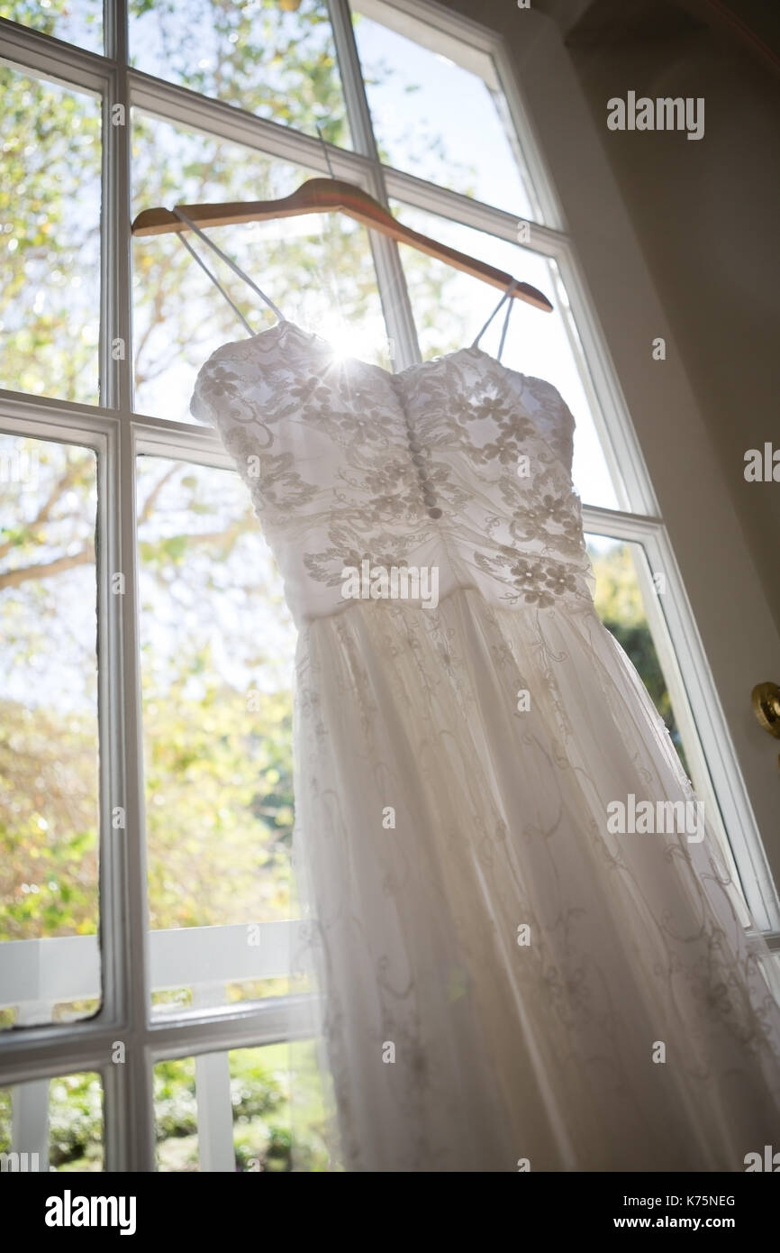 Low angle view of wedding dress hanging on window in dressing room Stock Photo