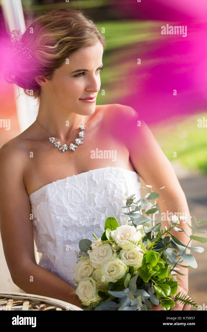 High angle view of thoughtful bride with bouquet sitting on chair in ...