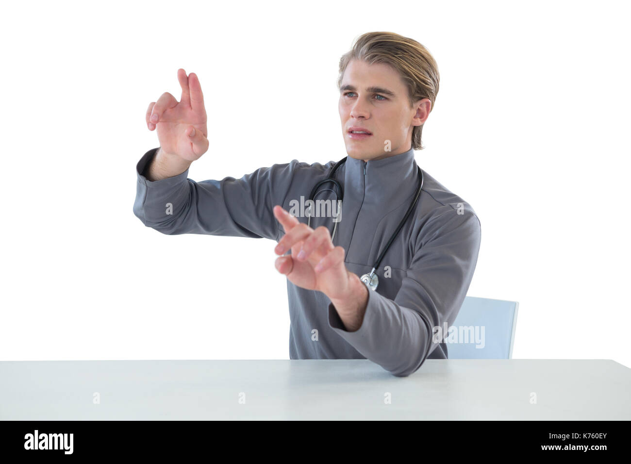 Male doctor touching imaginary interface screen while sitting at table against white background Stock Photo