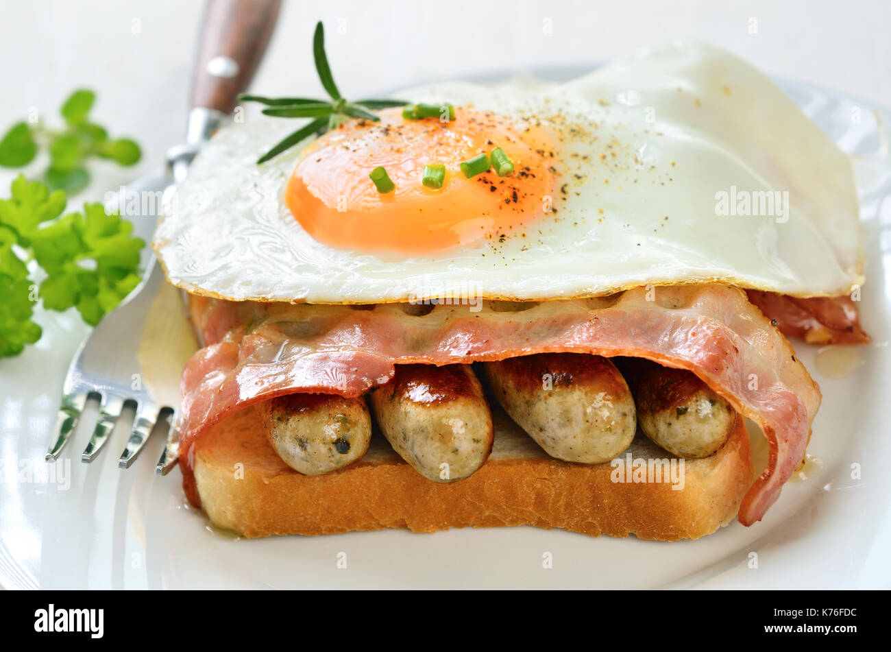 Toast with fried egg, sausages and bacon, garnished with rosemary