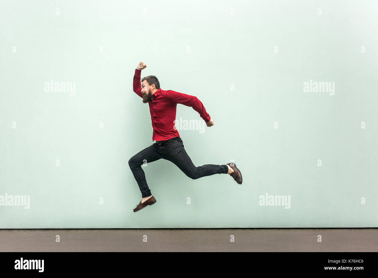 Was late for work in firs day. Young adult bearded man running to the work. Outdoor, gray wall Stock Photo