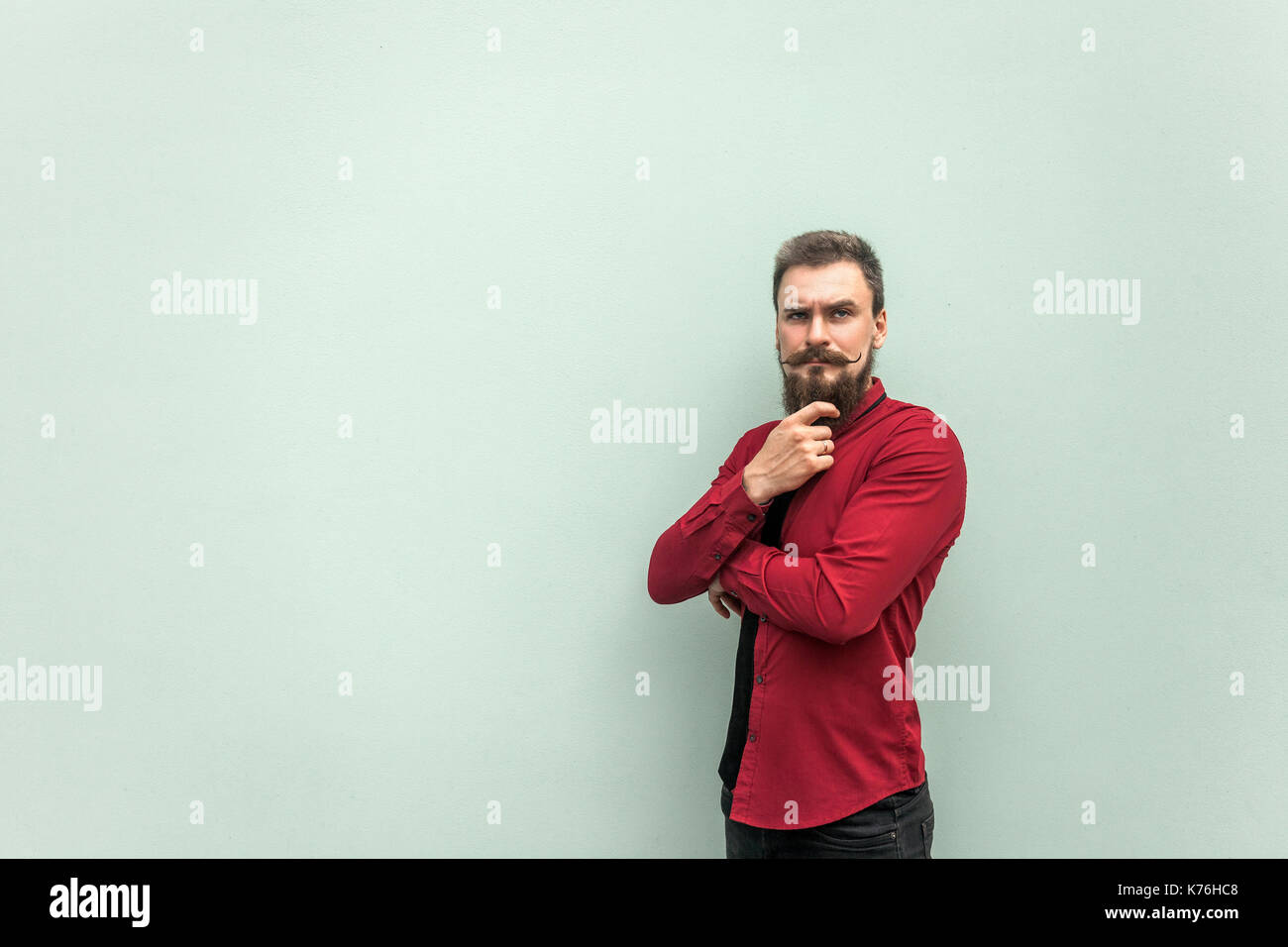 Thinking. Young adult bearded businessman touching chin and thinking. Studio shot. Isolated on gray background. Stock Photo