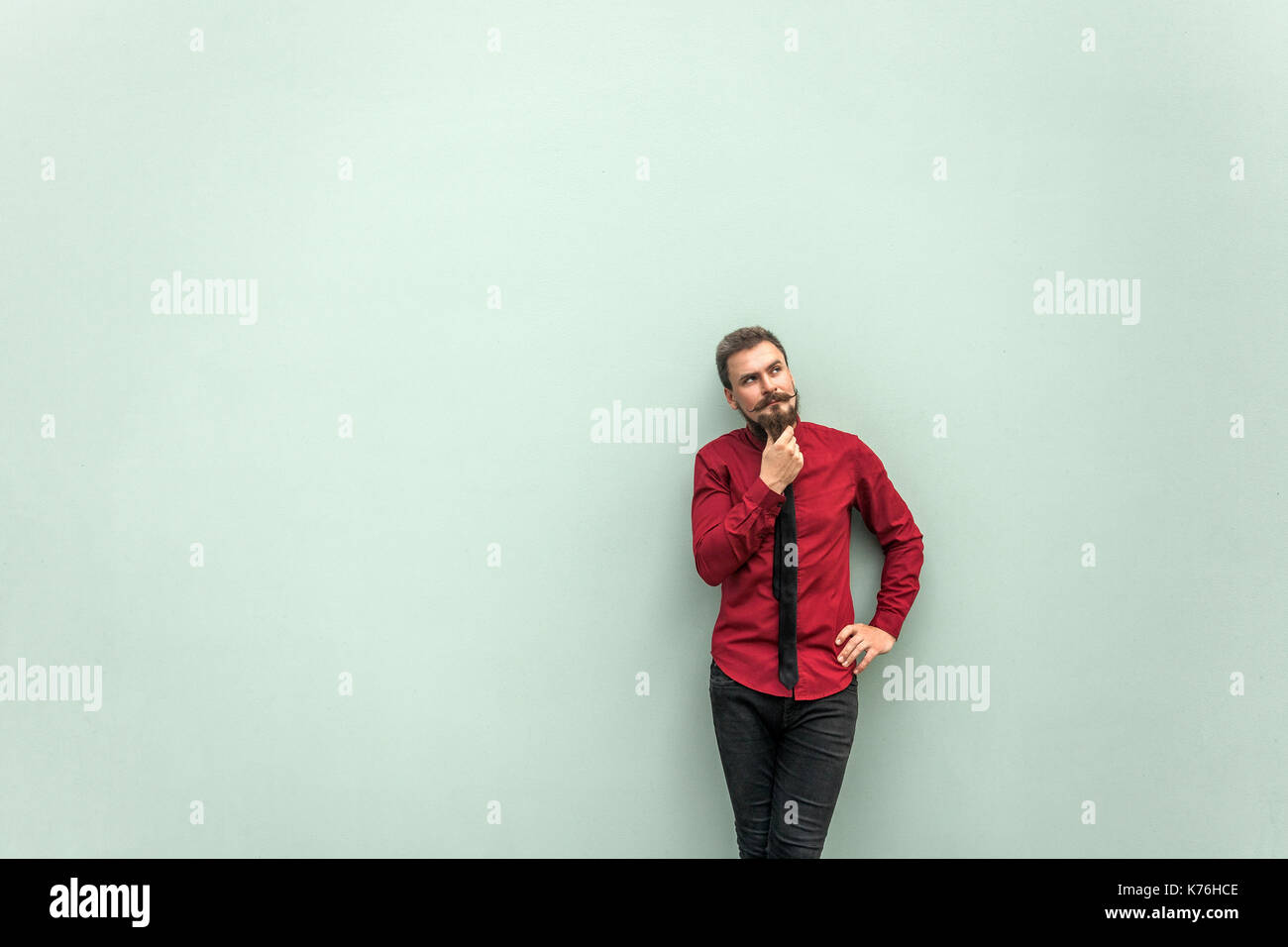 Thinking people . Young adult bearded worker touching chin, thinking and looking up. Studio shot. Isolated on gray background. Stock Photo