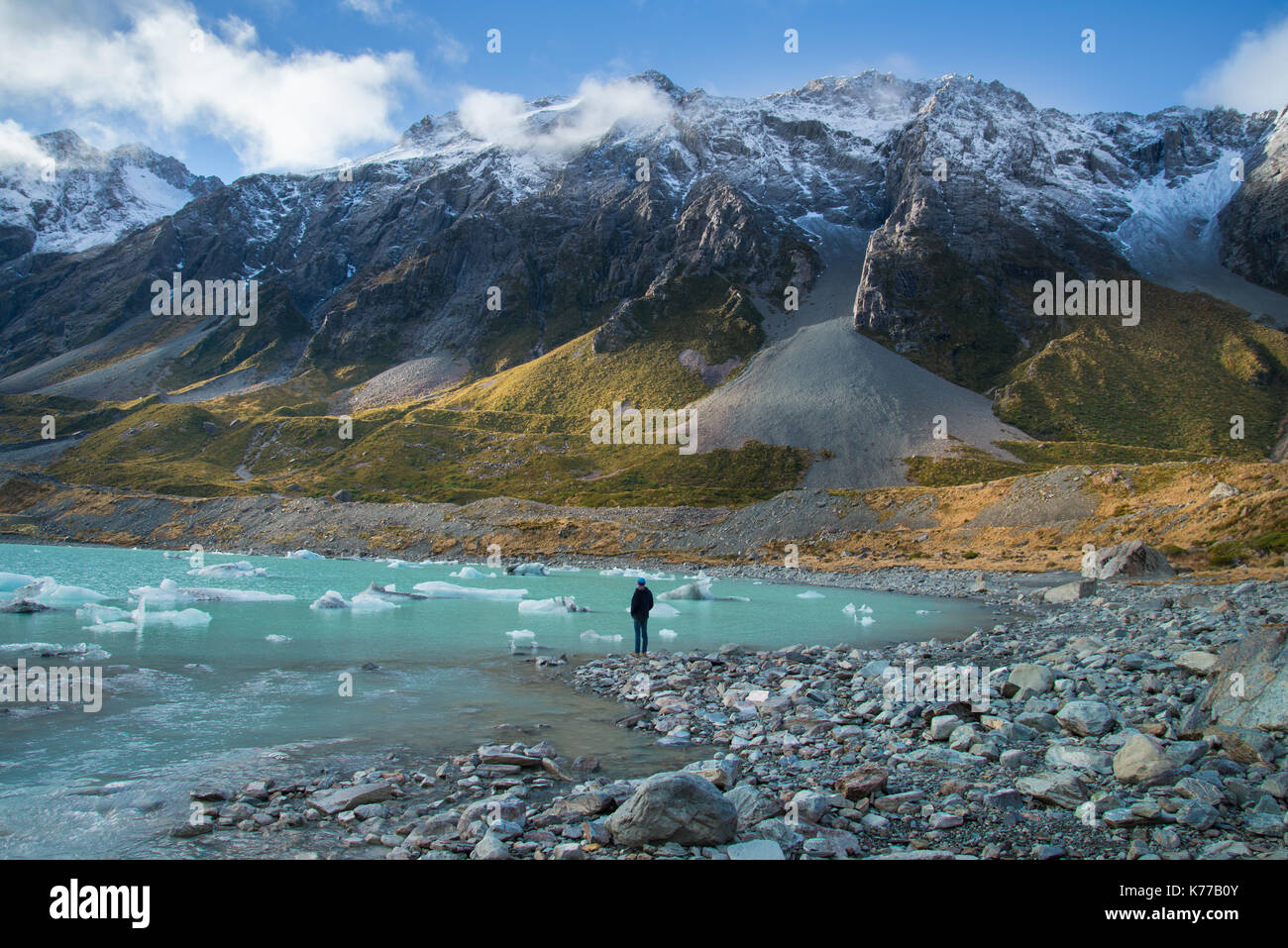 person at alpine lake surrounded by mountains and icebergs Stock Photo