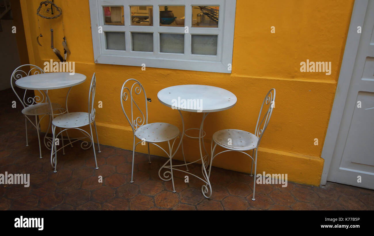 Two chairs and a small white metal round table with a yellow wall background inside a house Stock Photo