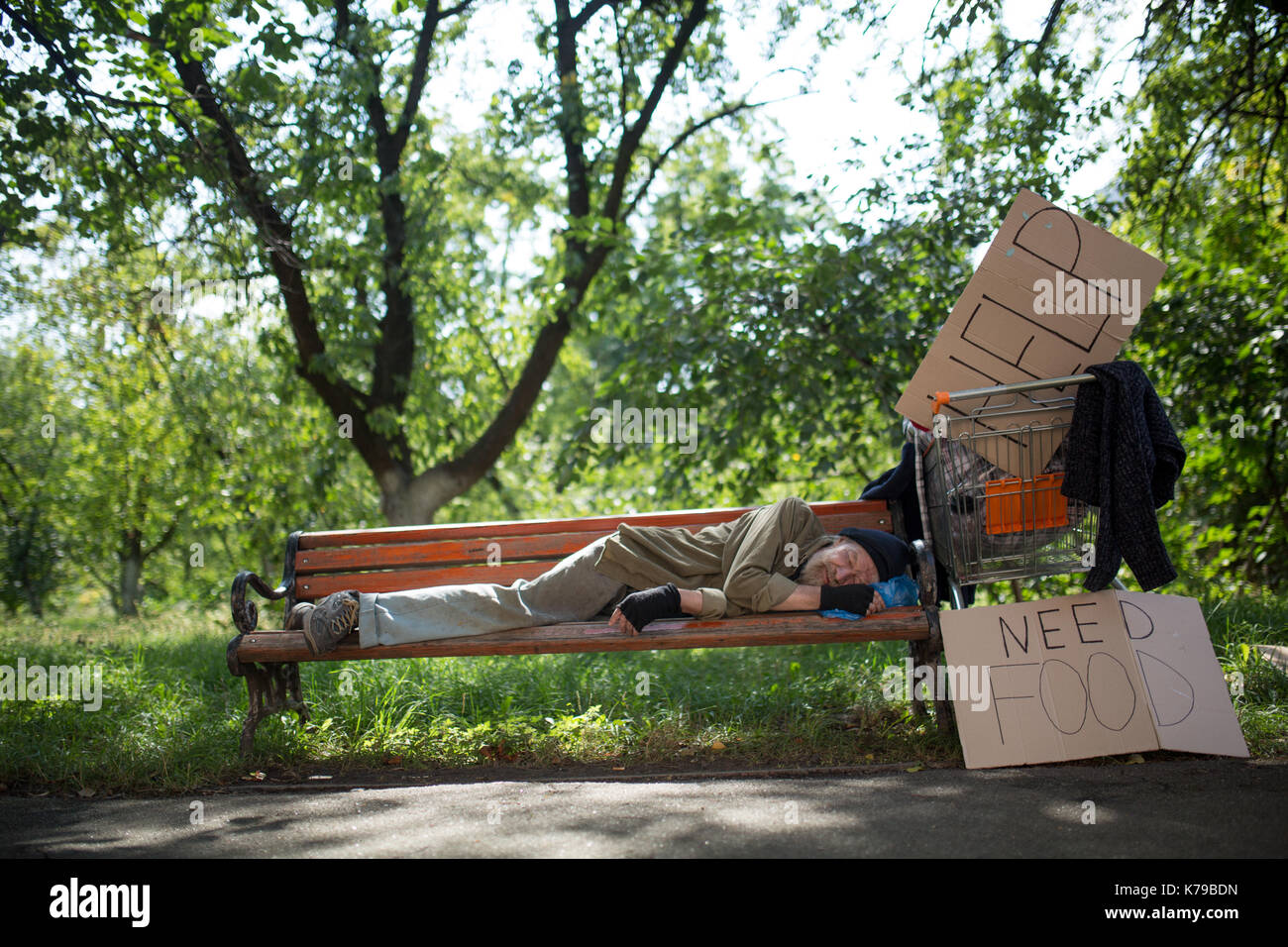 Homeless old man on the bench in city park. Stock Photo