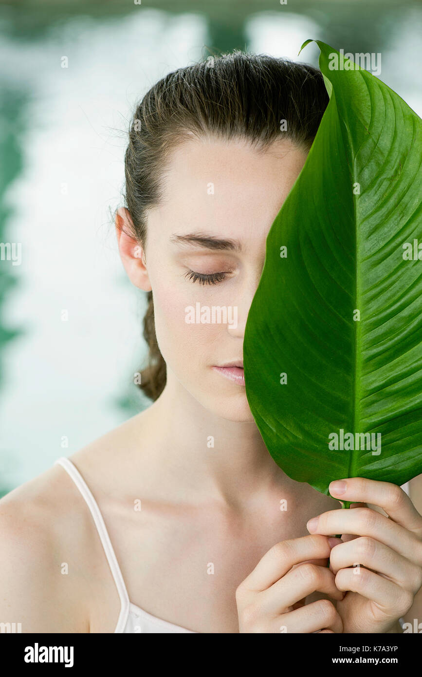 Young woman holding large leaf over half of her face, portrait Stock Photo