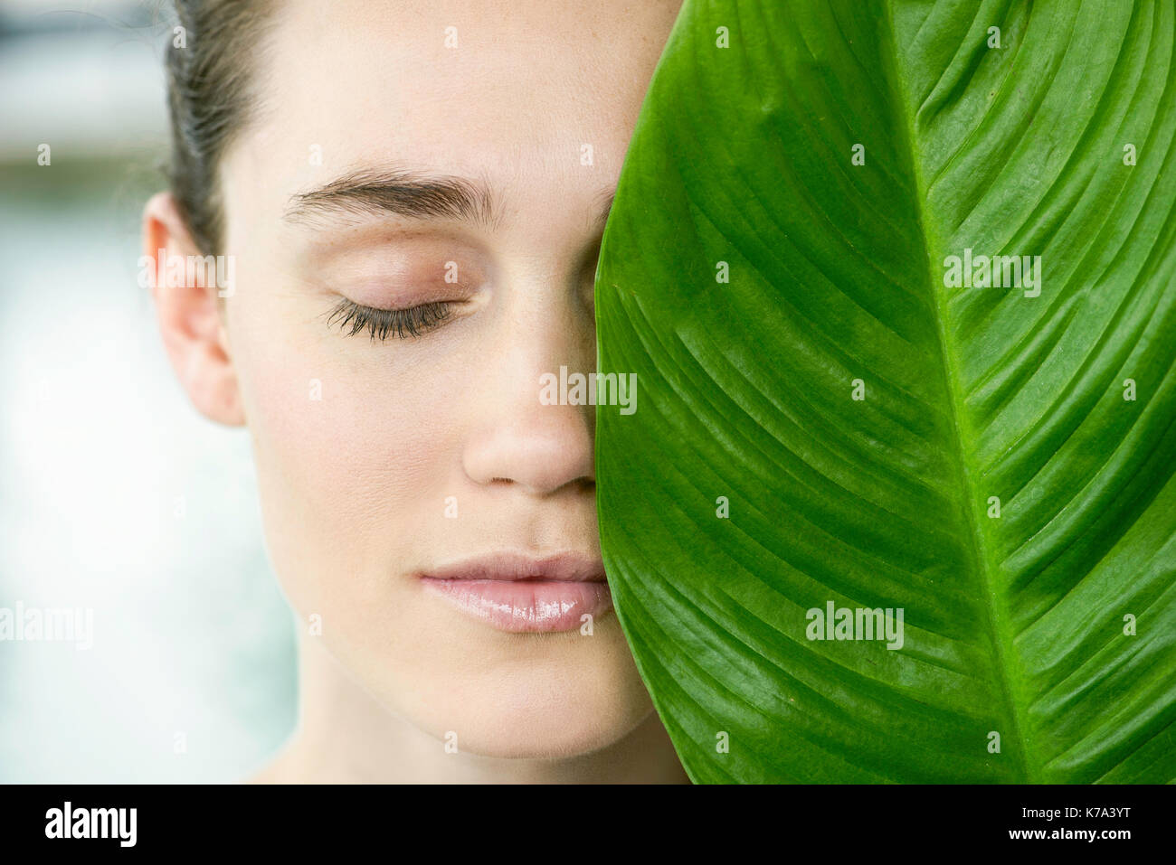 Young woman holding large leaf over half of her face, portrait Stock ...