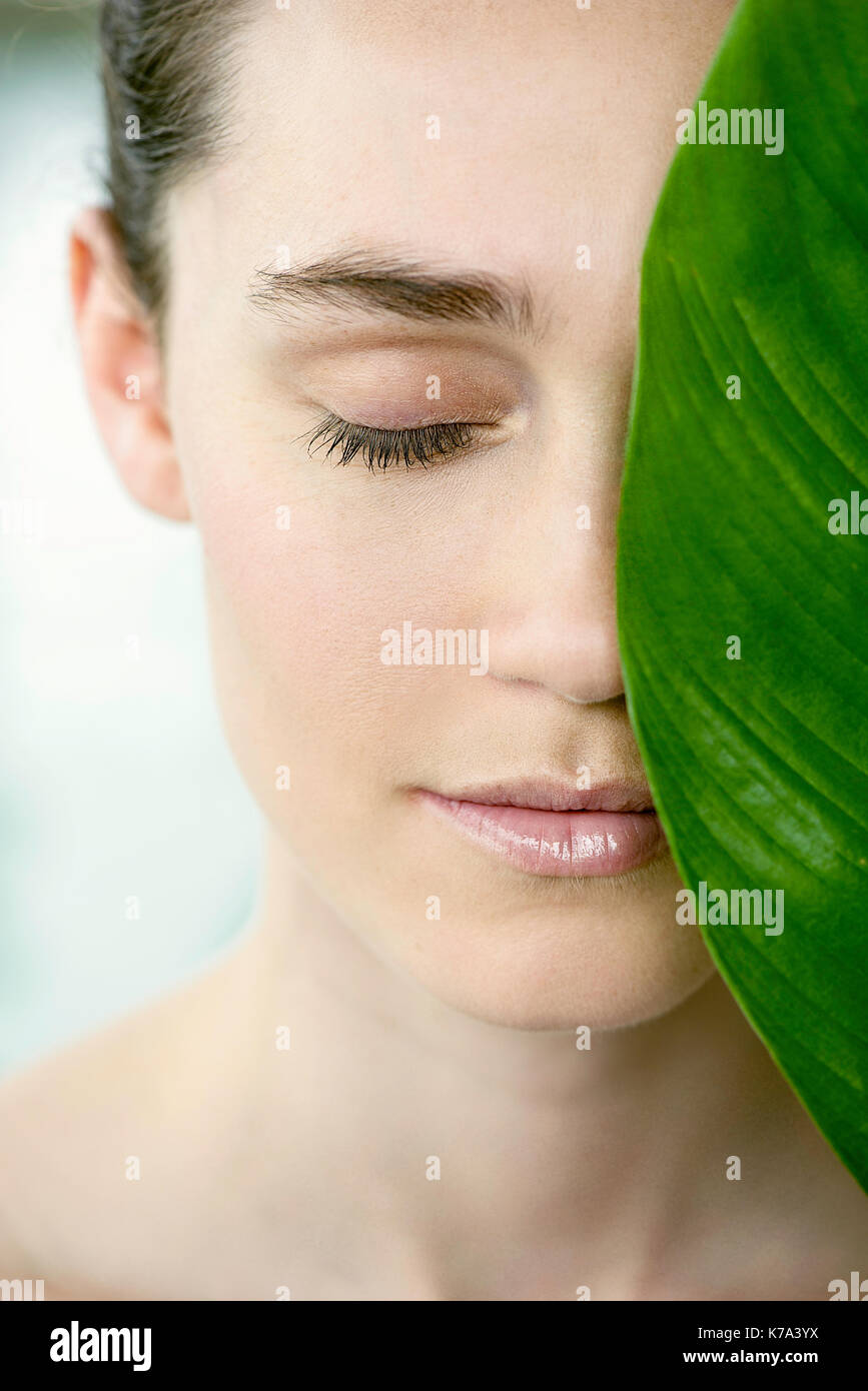 Young woman holding large leaf over half of her face, portrait Stock ...