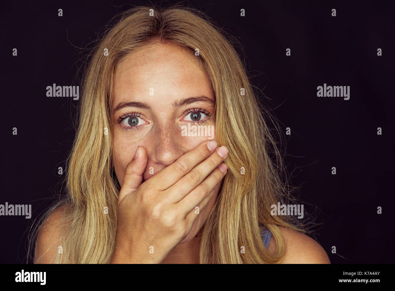 Young woman with wide eyes and hand covering mouth Stock Photo