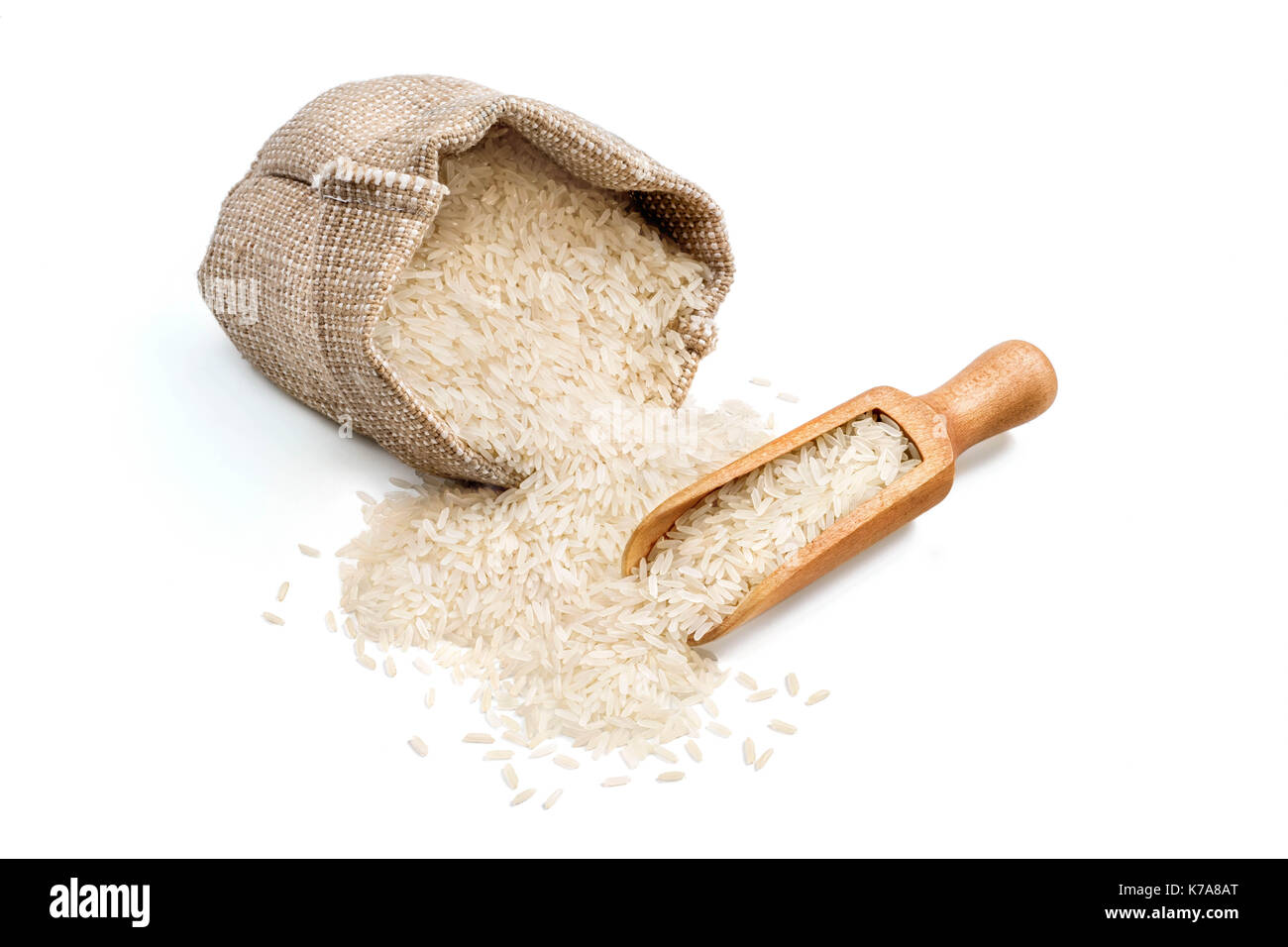 Parboiled rice scattered from burlap sack and wooden scoop isolated on white background. Healthy food. Close up, high resolution product Stock Photo