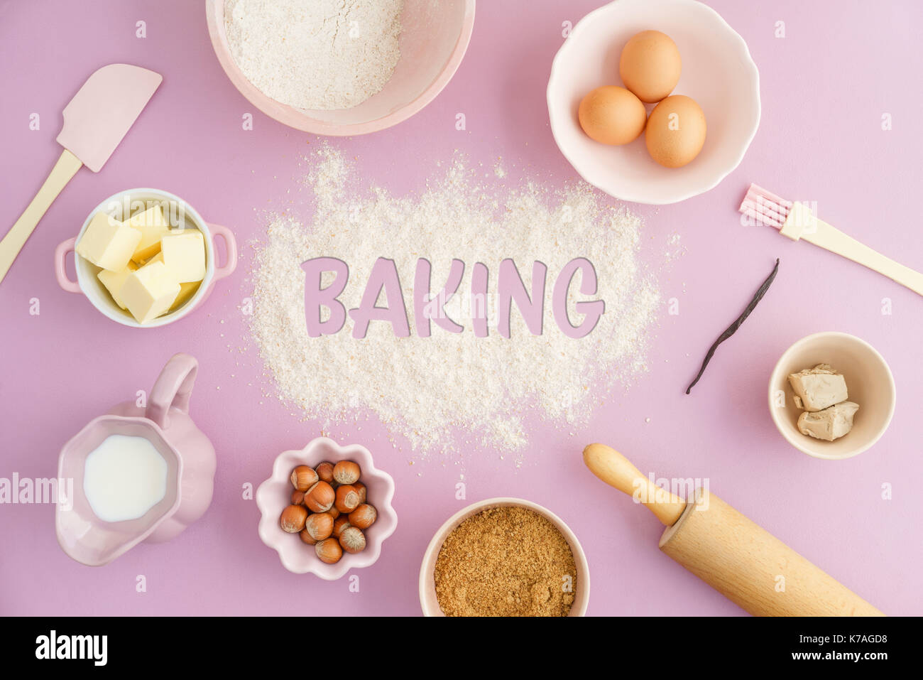 Flatlay collection of tools and ingredients for home baking on pink background with the word baking written in flour in the center. Shot from above Stock Photo