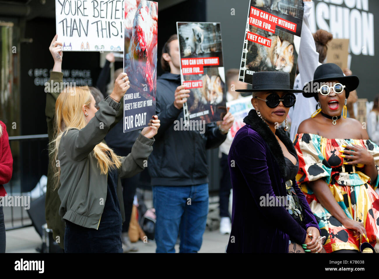 15/09/2017 London, UK. London Fashion Week SS18 and Animal rights activists demonstrating outside British Fashion Council show space during London Fashion Week SS18. Two fashionistas posing for photographers. One of the fashion girls is wearing a fur coat. Animal rights activists noticed that girl is wearing a fur and surrounded girls with a posters with animal cruelty for fur. However two girls only giggle at animal rights activists and continue posing for cameras. Stock Photo
