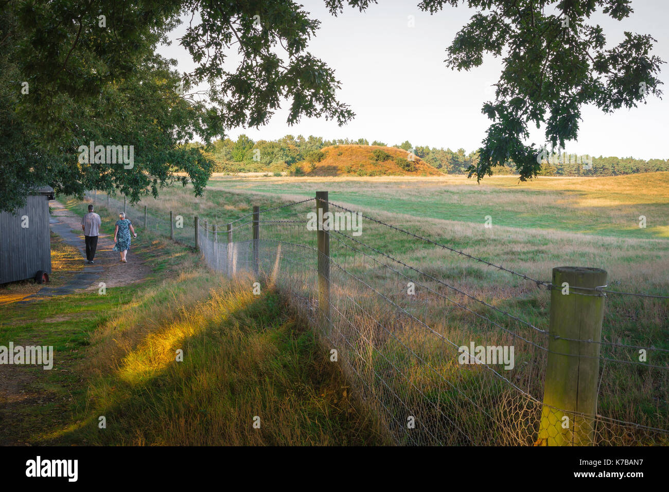 Sutton Hoo Suffolk, view of a middle aged couple walking on a visitors' path with an Anglo Saxon burial mound in the background, Suffolk, England. Stock Photo
