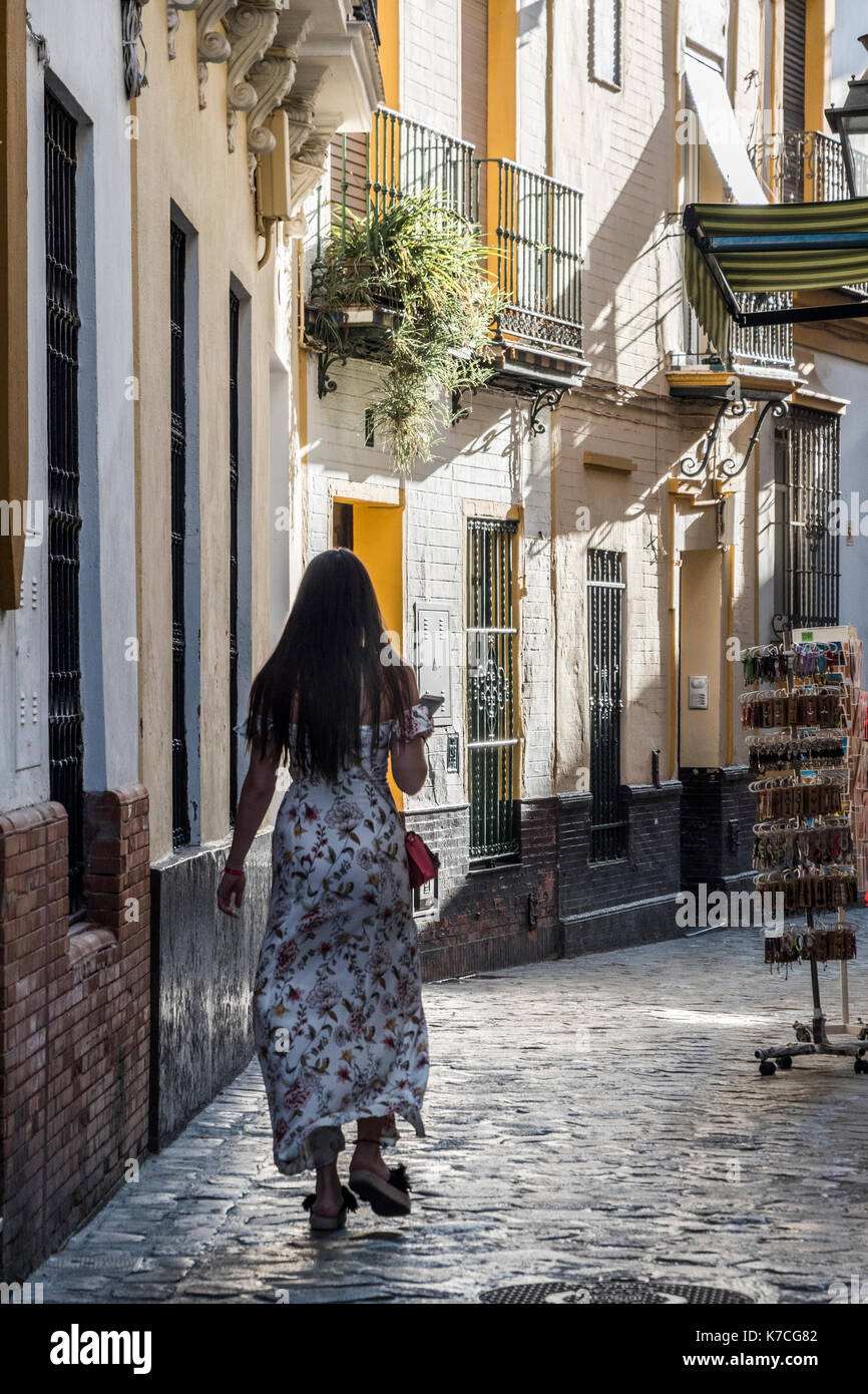Young girl with long dress walking along typical street of Seville