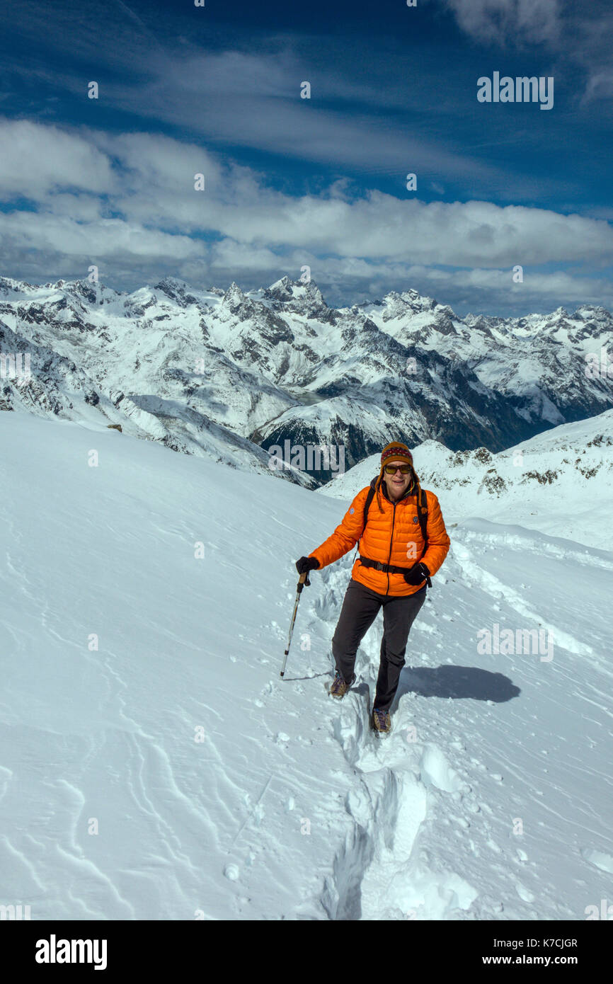 Female mountain walker on snow wearing orange duvet jacket Stock Photo