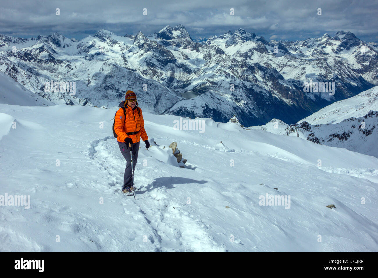 Female mountain walker on snow wearing orange duvet jacket Stock Photo