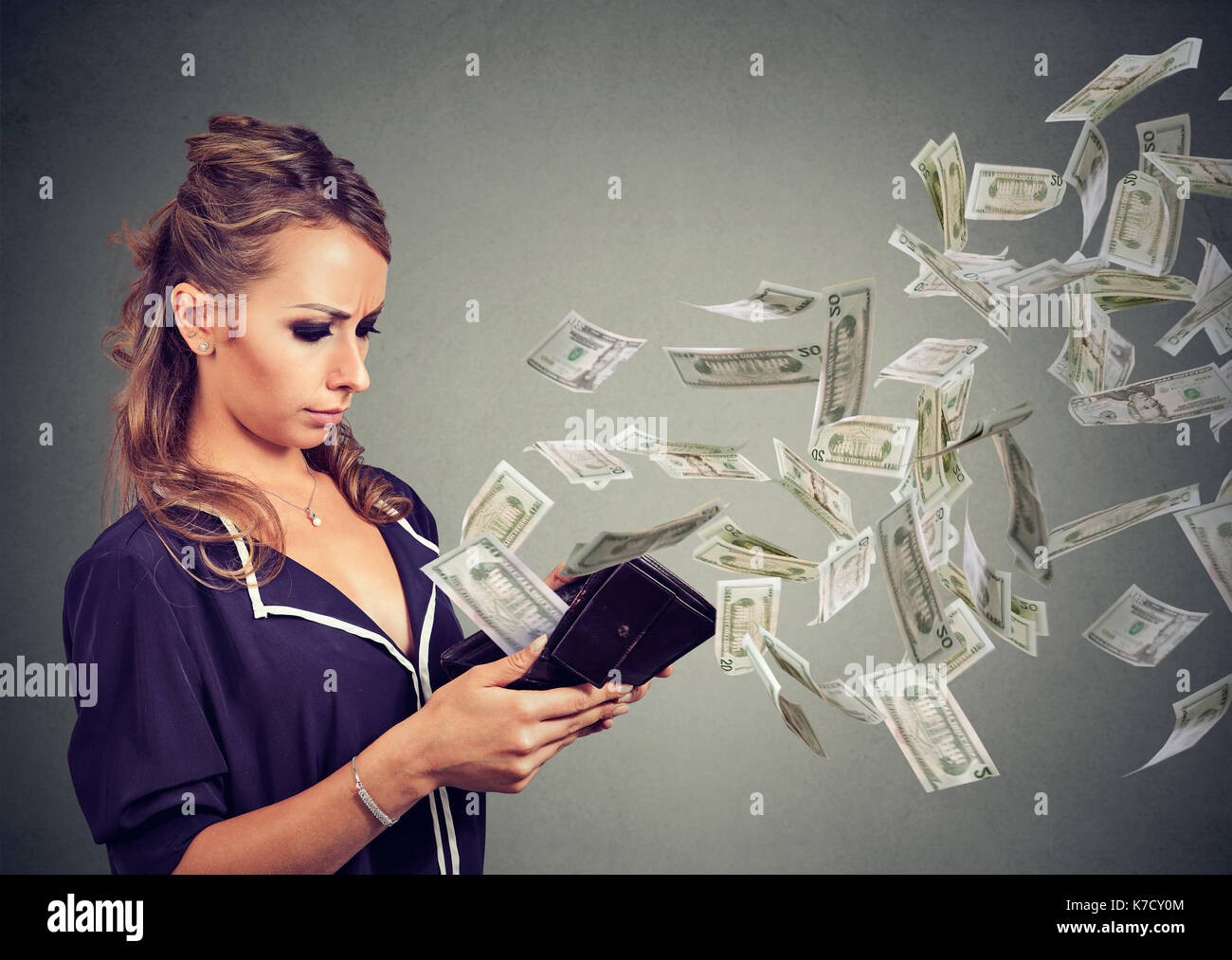 Sad woman looking at her wallet with money dollar banknotes flying out away Stock Photo