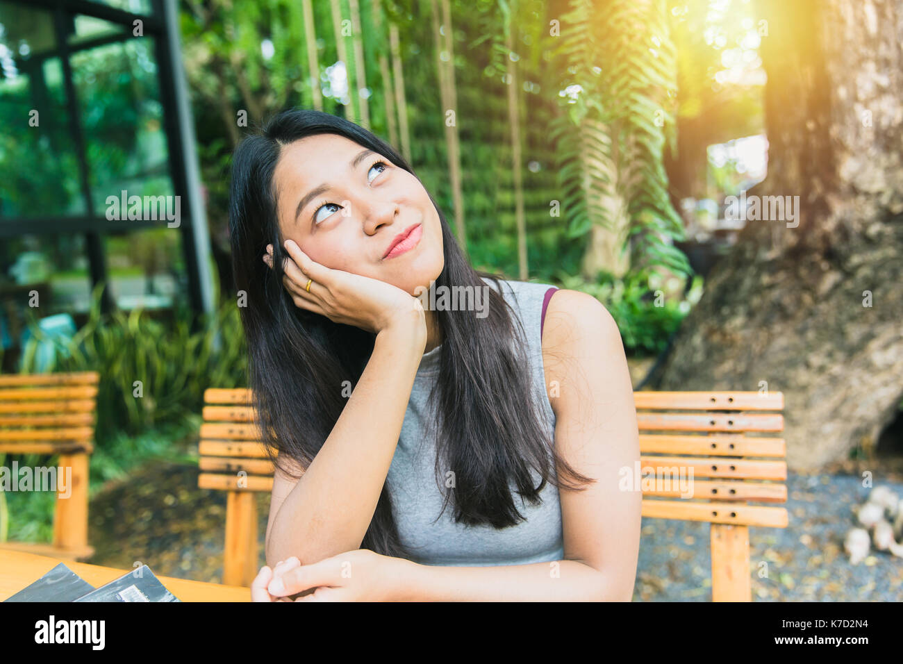 Thinking about or missing passed memory. Thai Asian women long hair hand chin rest and watching vision look out far away with sun light at cafe Stock Photo