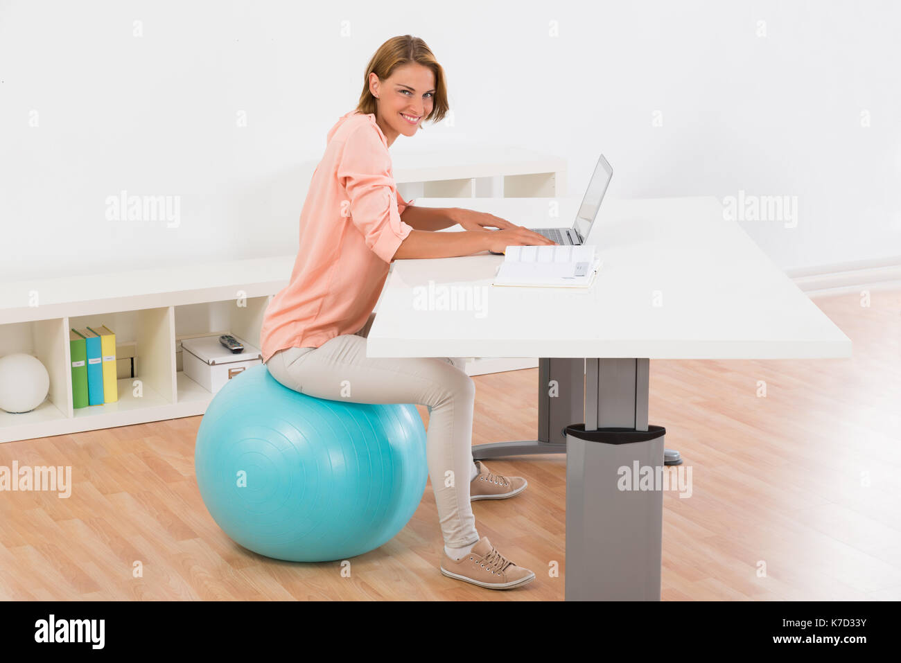 Young Woman Sitting On Blue Fitness Ball Using Laptop At Desk