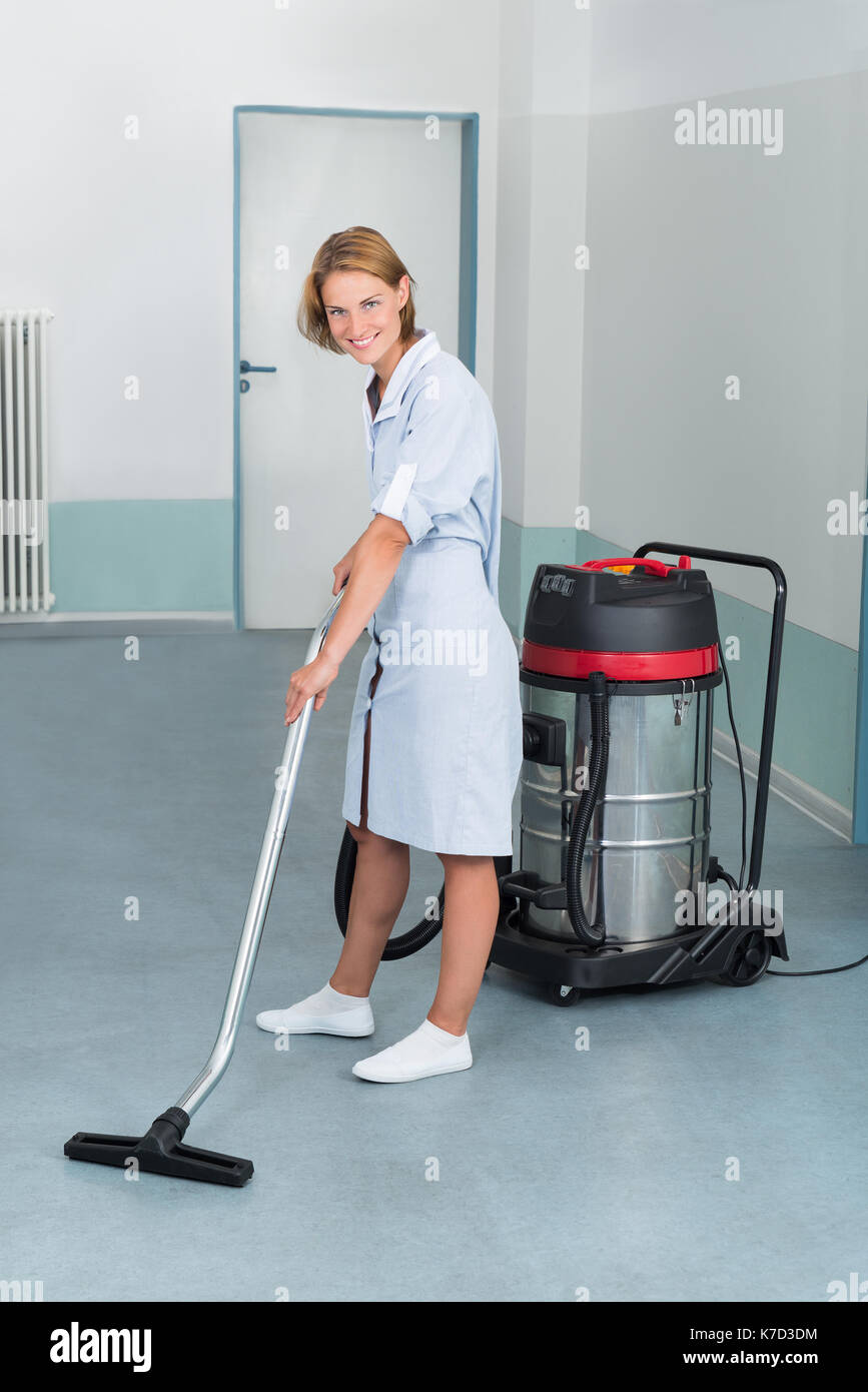 Young Female Cleaner In Uniform Vacuuming Floor Stock Photo