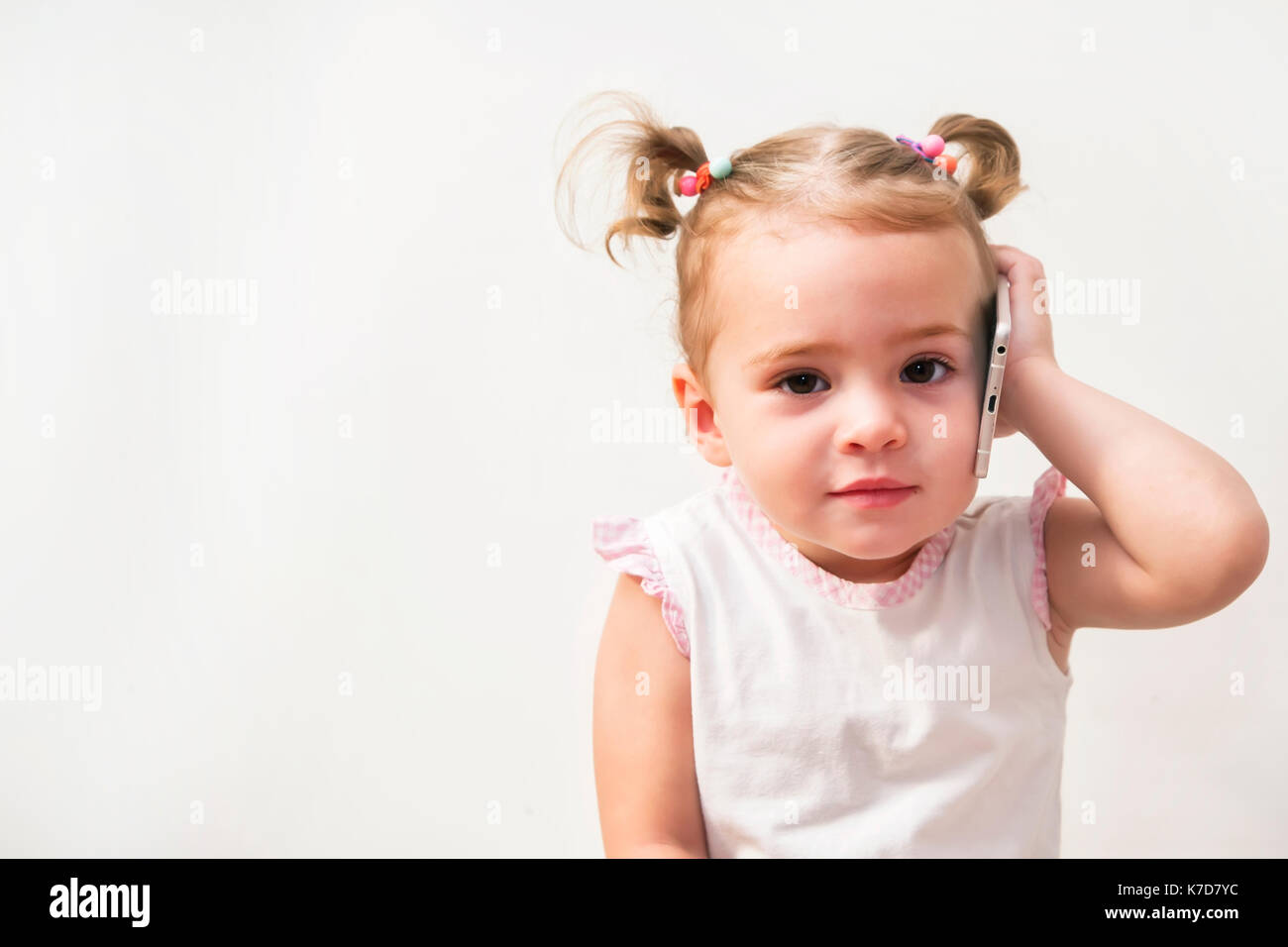 Baby girl speaking by cell phone, white background Stock Photo