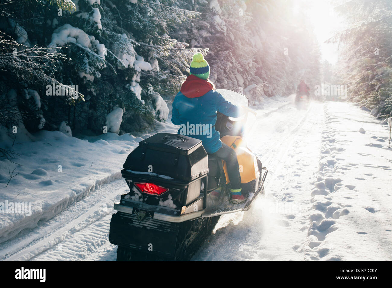 Rear view of woman riding snowmobile on snow covered field Stock Photo