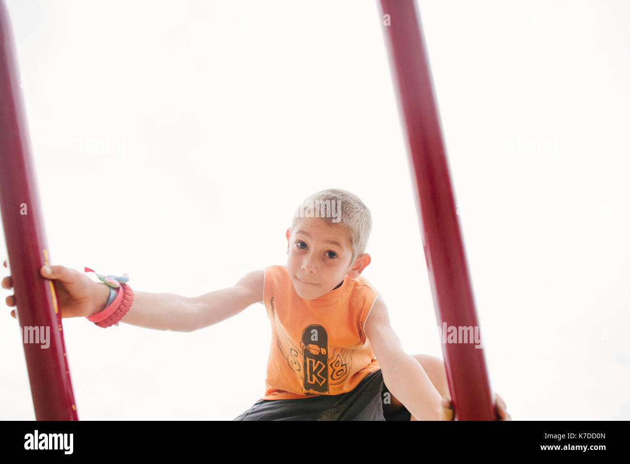 Low angle portrait of boy on outdoor play equipment against clear sky Stock Photo