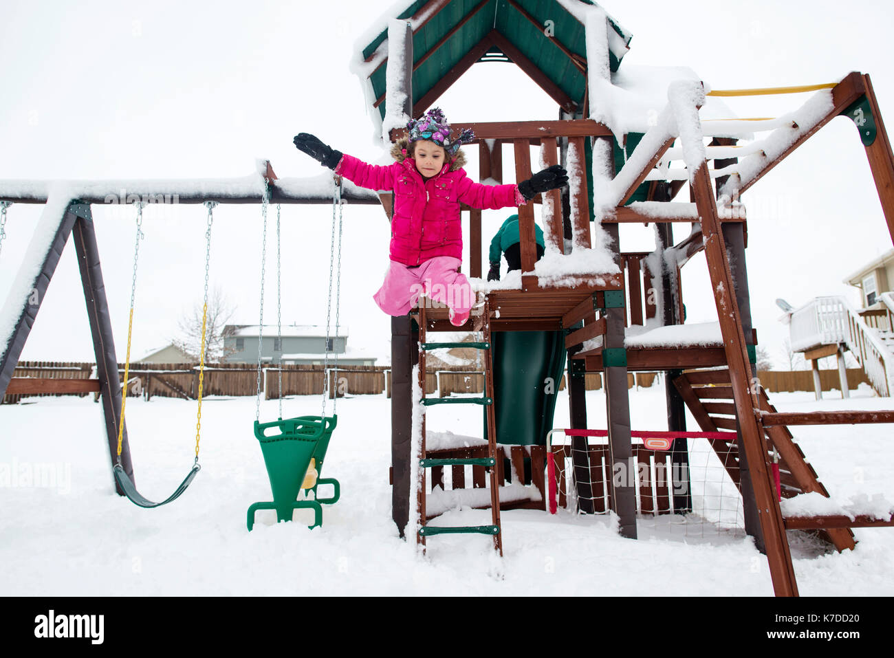 Playful girl jumping from outdoor play equipment at playground during winter Stock Photo