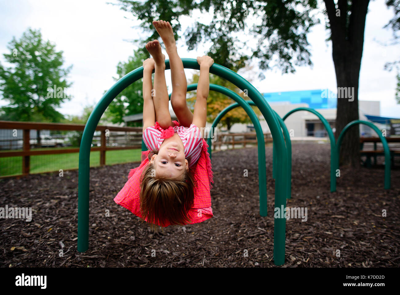Portrait of girl hanging upside down on outdoor play equipment at playground Stock Photo