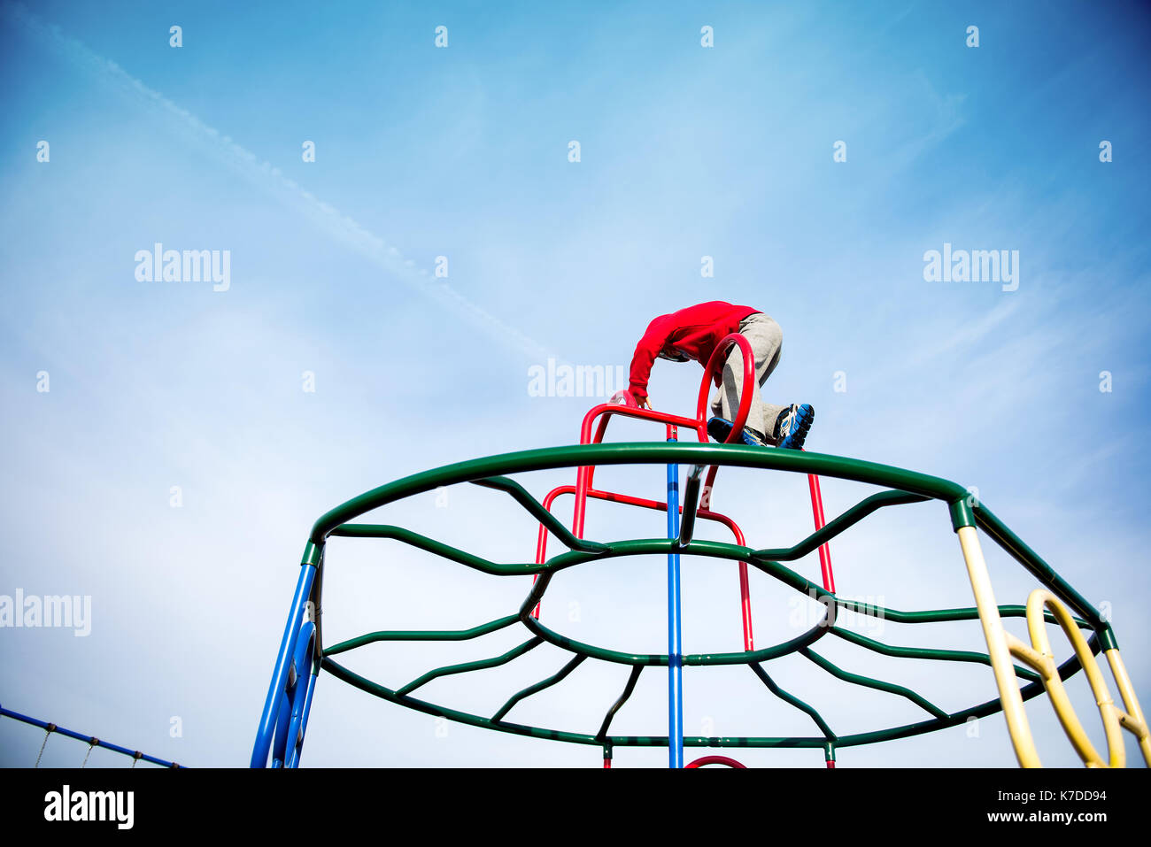 Low angle view of boy climbing on monkey bars against sky at playground Stock Photo