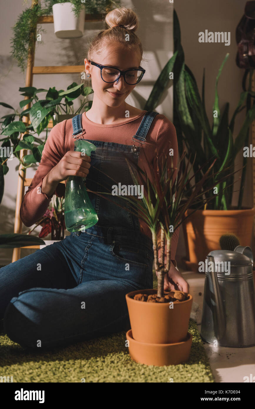 Happy woman watering potted plant at home Stock Photo