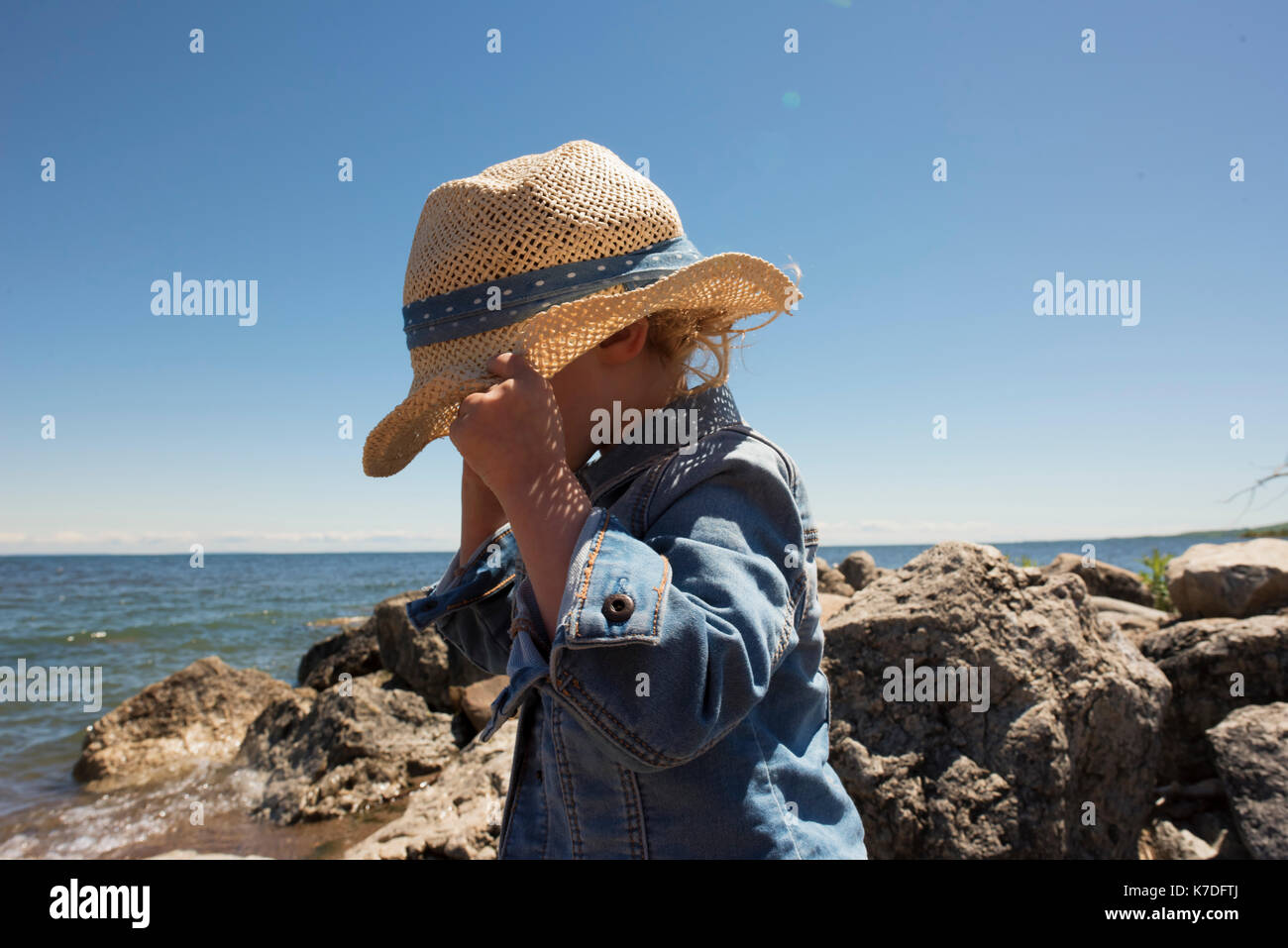 Side view of girl adjusting hat while standing on beach against clear sky Stock Photo