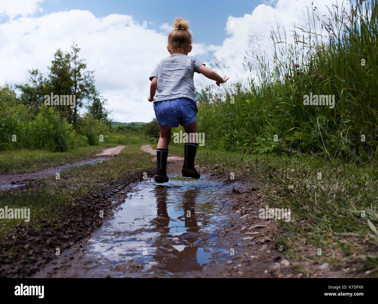 Little girl jumping high above big puddle of water. Bath Towel by