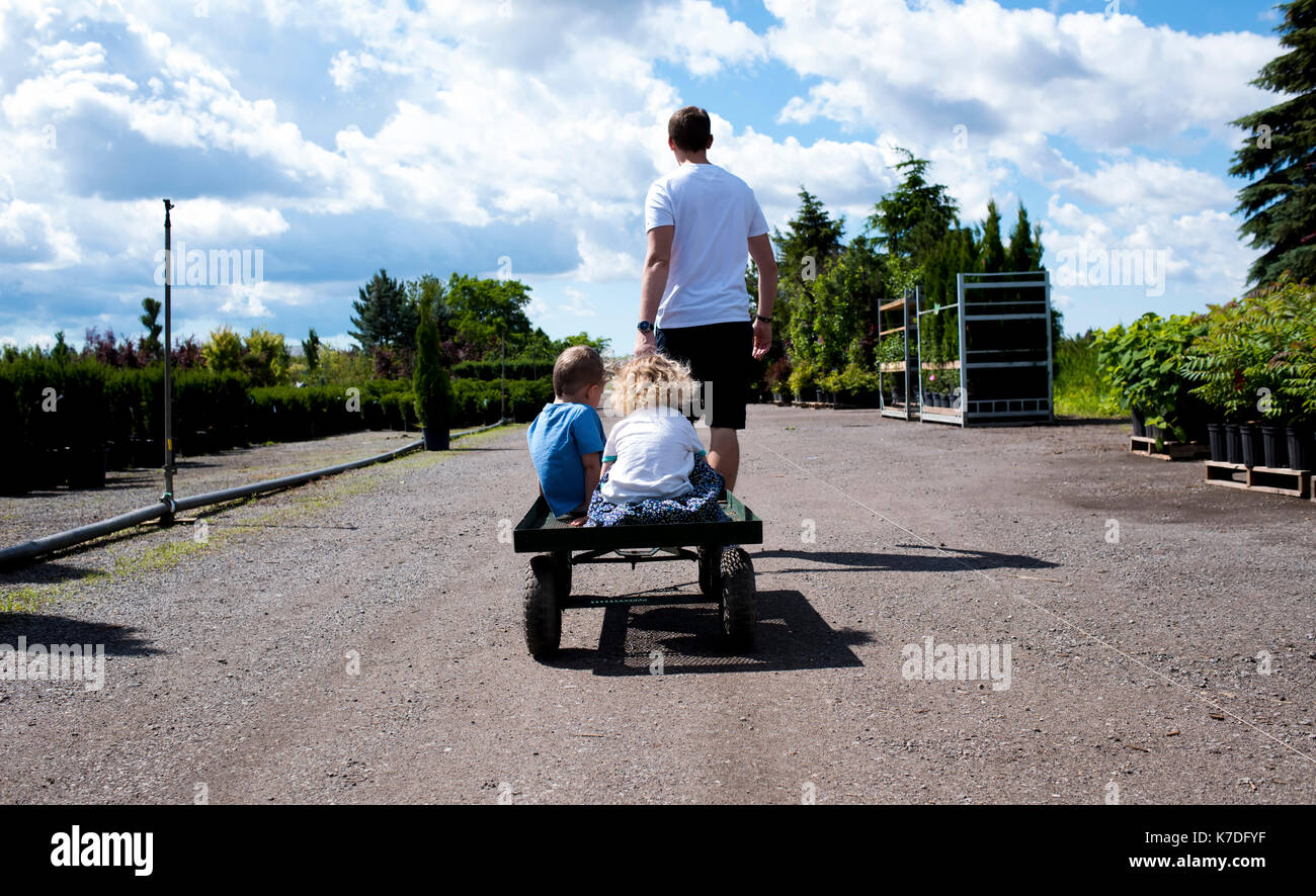 Rear view of father giving toy wagon's ride to children during sunny day Stock Photo
