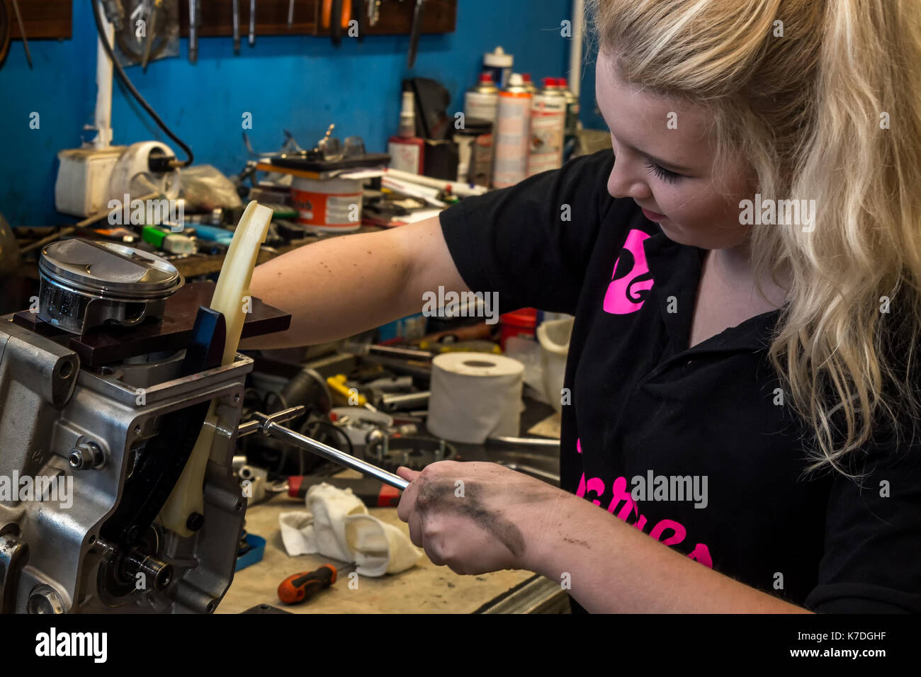 Young woman breaks stereotypes - doing male job at mechanical workshop. Repairing motorcycle engine Stock Photo