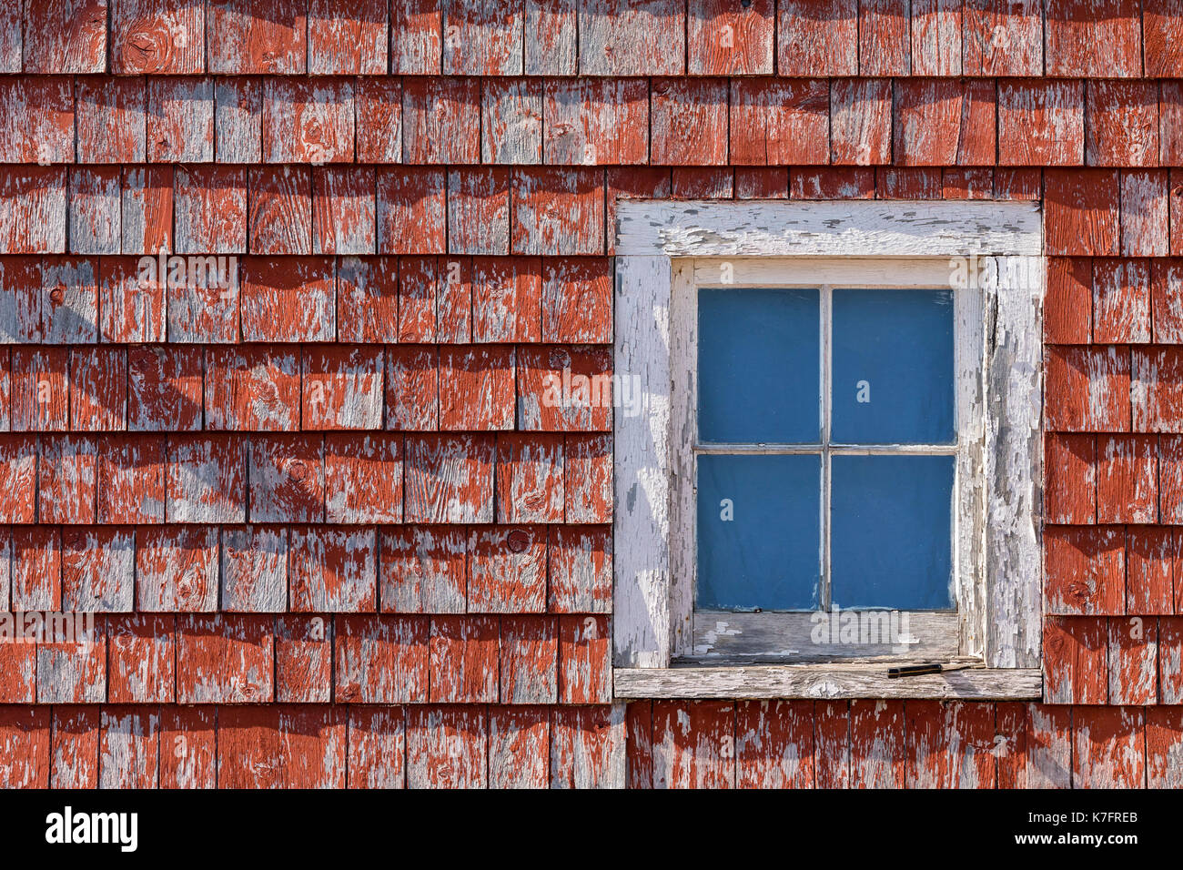 A small window in a small building with rustic red shake siding. Stock Photo