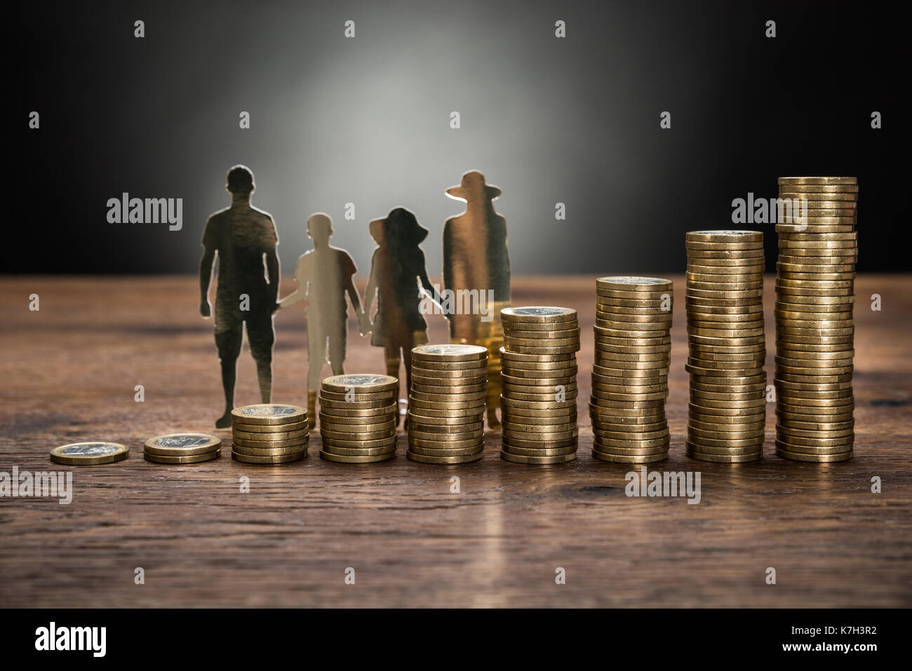 Close-up Of Paper Cutout Family With Stack Of Coins On Wooden Table Stock Photo
