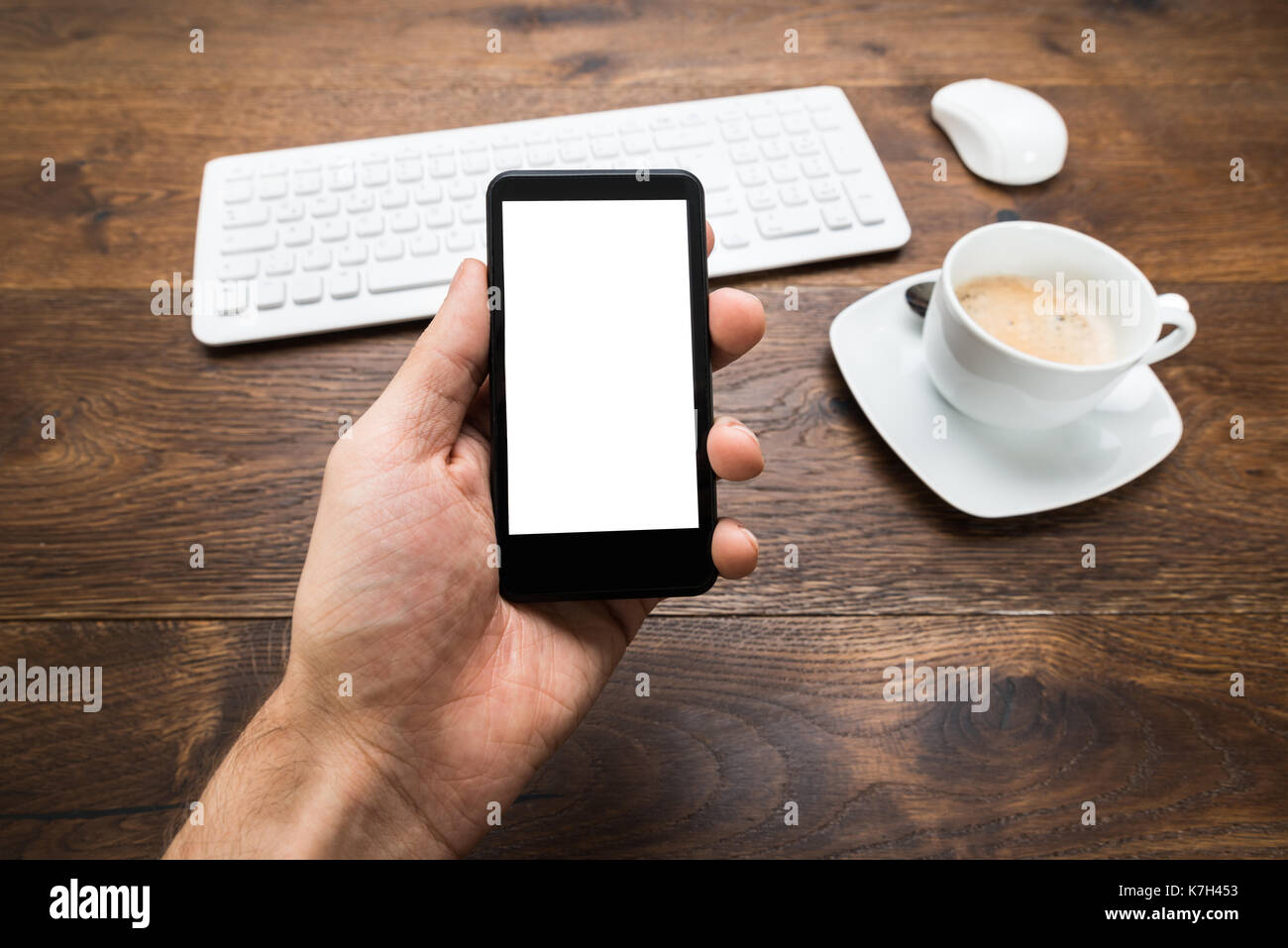 Close-up Of Person Hand Holding Mobile Phone With Cup Of Tea On Desk Stock Photo