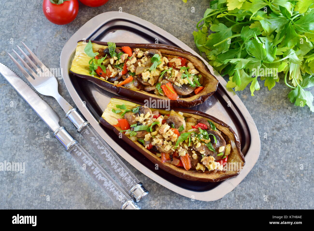 Eggplants stuffed with mushrooms, onions, carrots, tomatoes and nuts on a metal plate on a grey background. Vegetarian food. healthy eating concept. Stock Photo