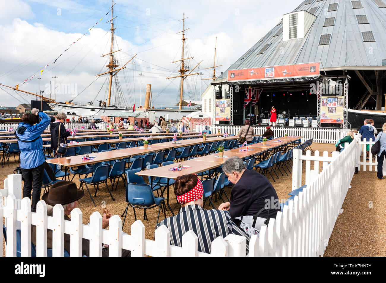 Fenced off area with long rows of tables leading to a stage where a woman in red is singing. Only a few people there so venue looks empty. Event during the popular Salute to the 40s weekend at the Chatham historic Dockyard. Stock Photo